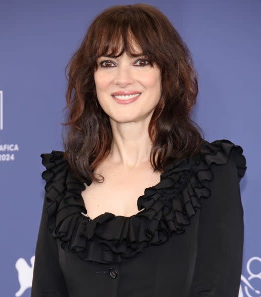 Person in elegant ruffled dress stands in front of a blue event backdrop, smiling