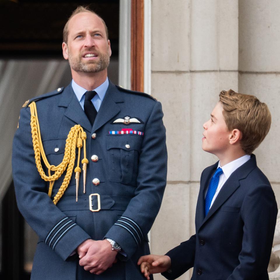  Prince William wearing a blue military coat looking up and standing next to Prince George . 