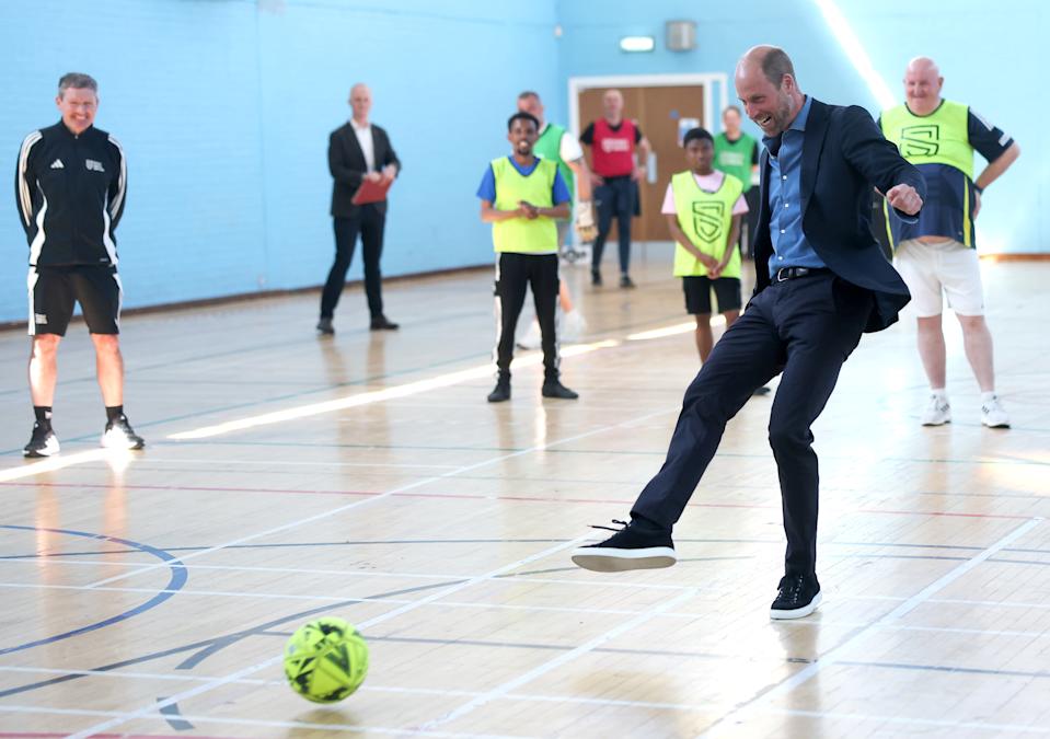 Prince William kicking a soccer ball in a suit