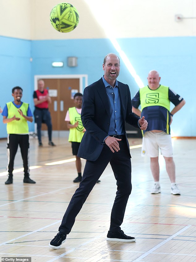 Prince William, Prince of Wales laughs as he plays football during a visit as The Royal Foundation launches a new community impact partnership with Street Soccer Scotland at Leith Community Centre