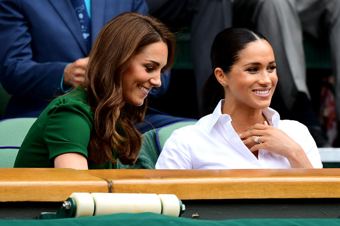 Kate Middleton and Meghan Markle sitting together at an outdoor event, smiling and engaged in conversation. Kate Middleton and Meghan Markle sitting together at an outdoor event, smiling and engaged in conversation.
