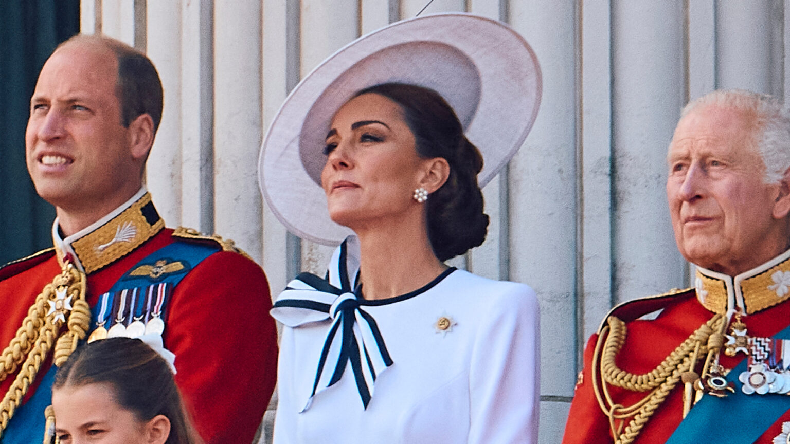 King Charles Concerned About Kate Middleton and Prince William Postponement Prince William and King Charles wear red military uniform and Kate Middleton wears a white dress with navy accents and a matching hat on the Buckingham Palace balcony