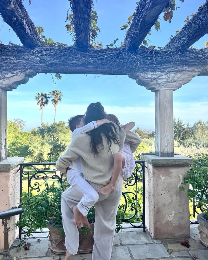 Meghan Markle cuddling her two chidlren wearing a pair of beige trousers and a matching cardigan