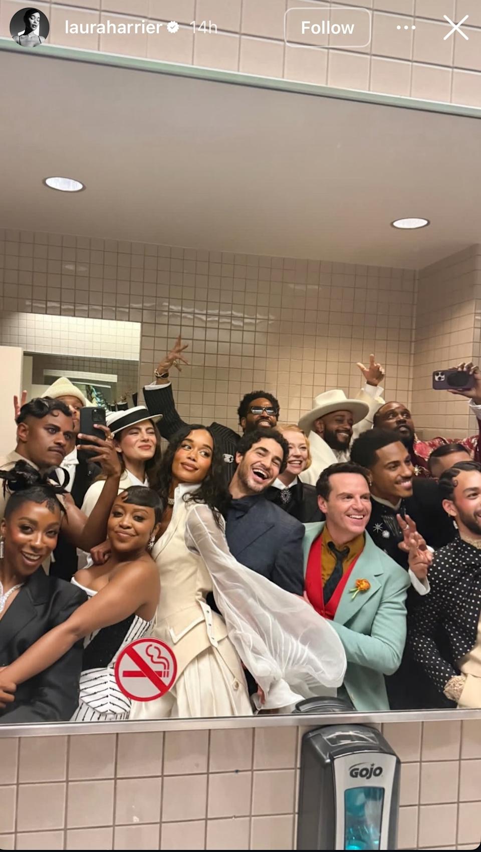 Group of people in a bathroom selfie at an event, dressed in formal and stylish attire, some wearing hats and accessories, smiling and posing
