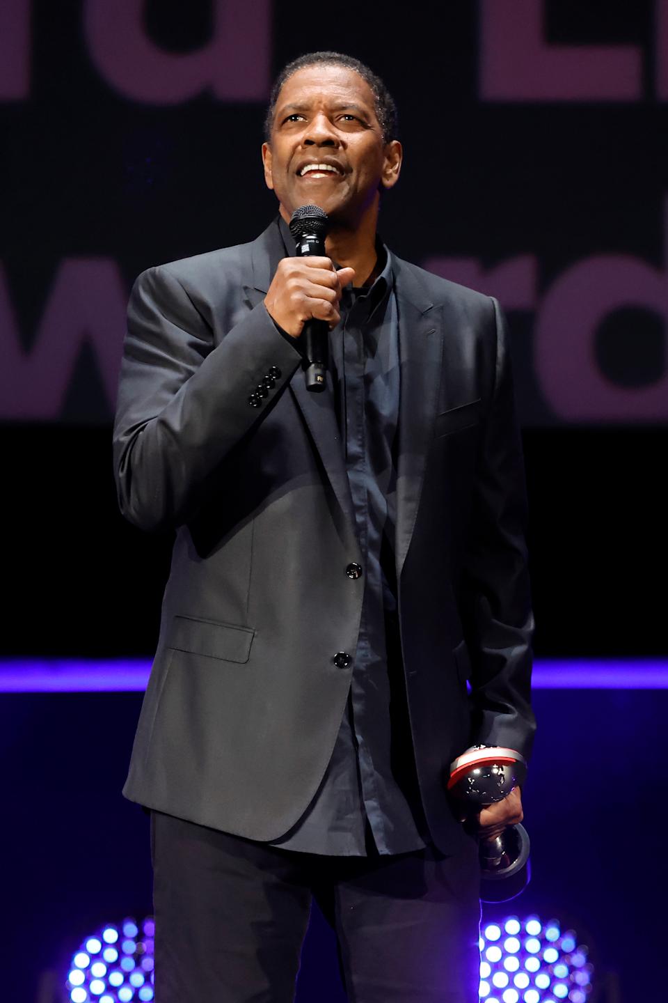 Denzel Washington holding an award, smiling on stage during an event