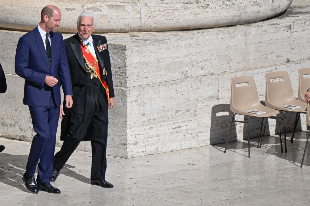 Prince William in a blue suit walking alongside a man in a black suit