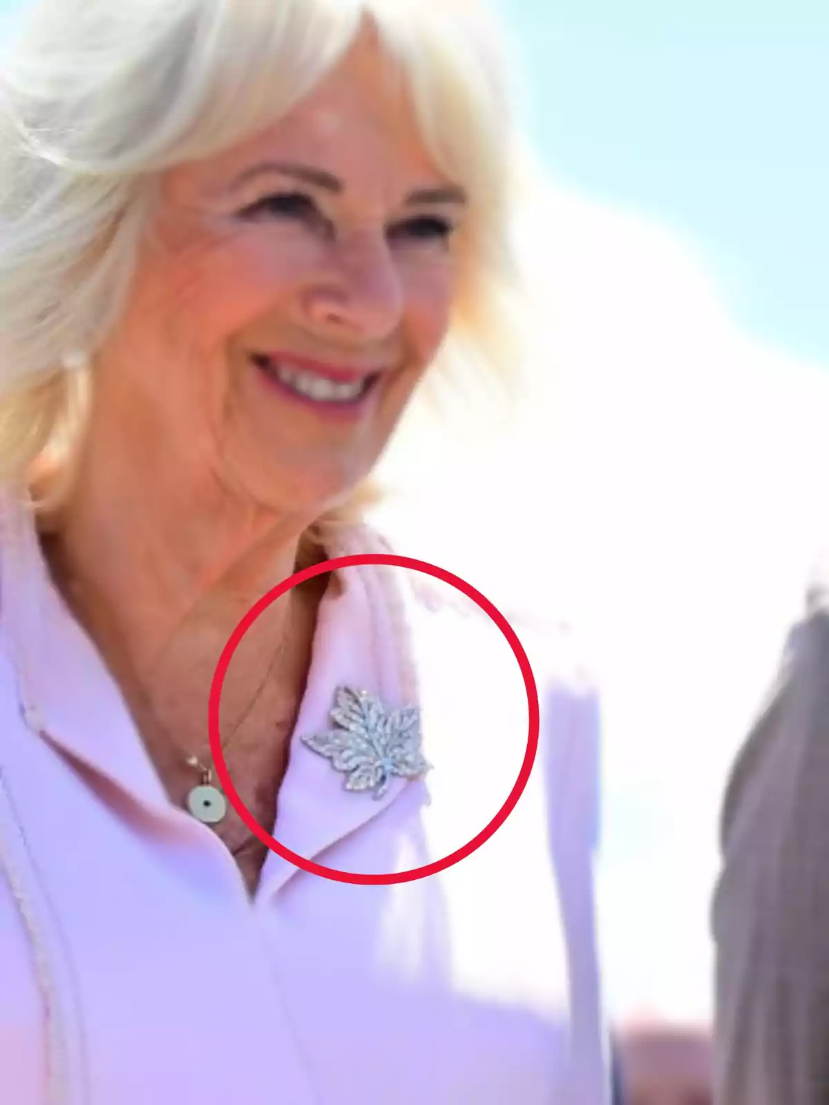Blonde-haired woman in light-colored clothing smiles while wearing a silver leaf-shaped brooch on her lapel