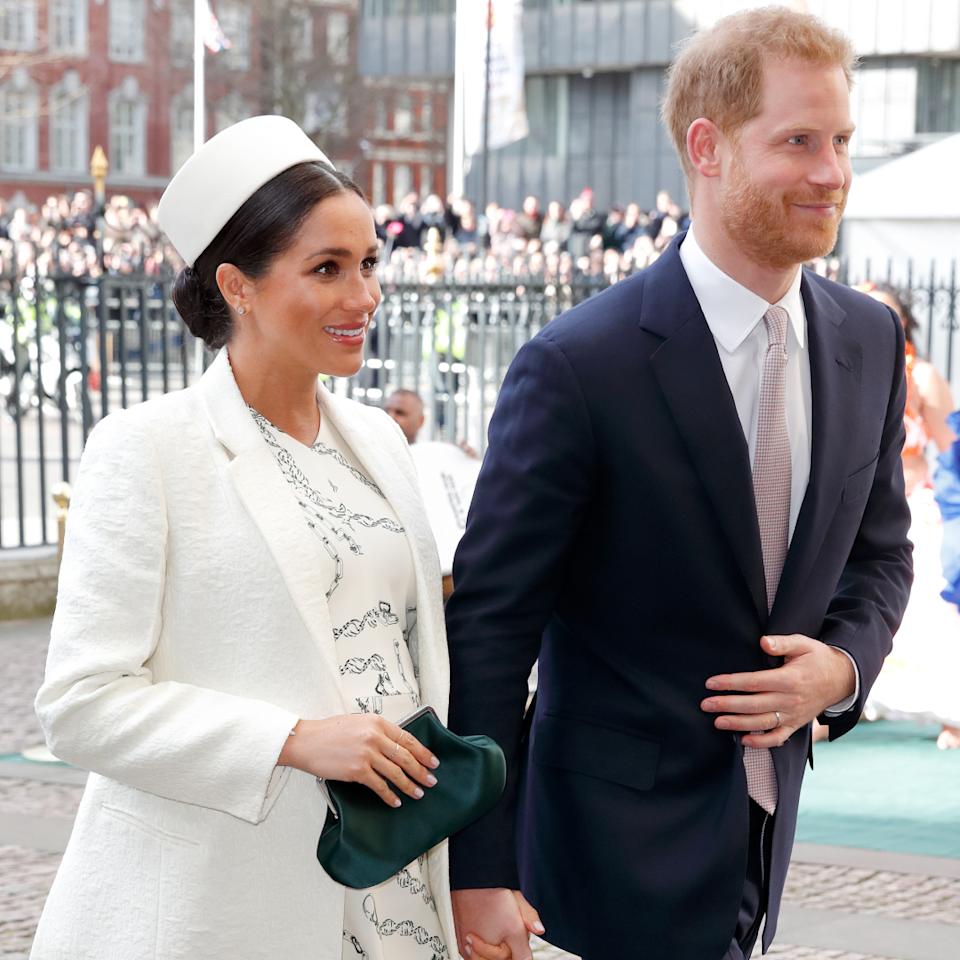 Meghan Markle wearing a white hat and coat holding hands with Prince Harry at Westminster abbey.
