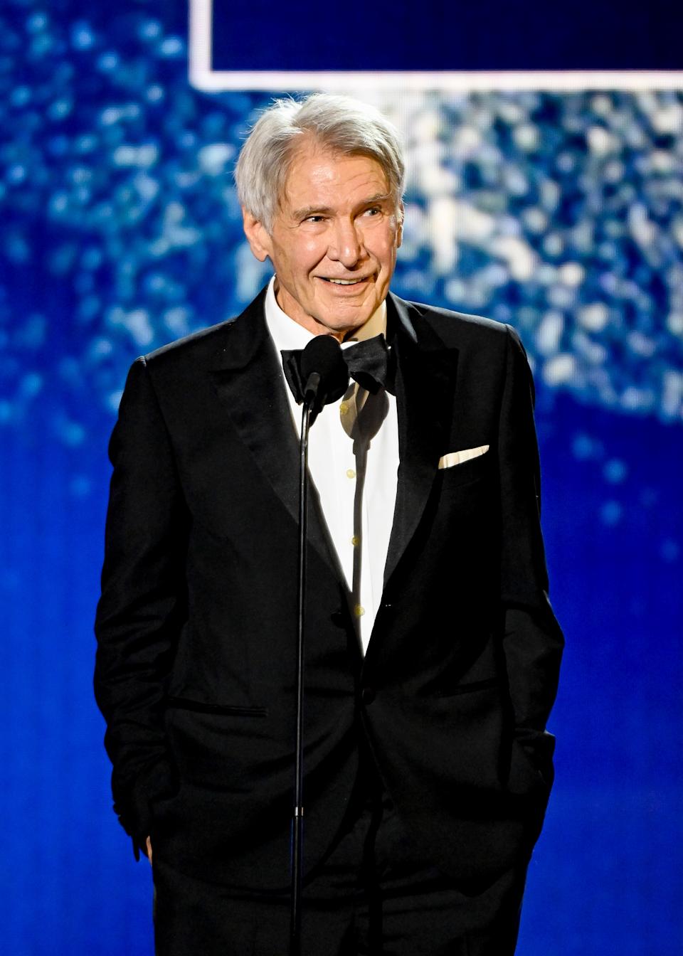 Harrison Ford smiling behind a microphone on stage