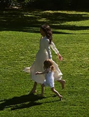 Meghan Markle and a child running on a grassy lawn.