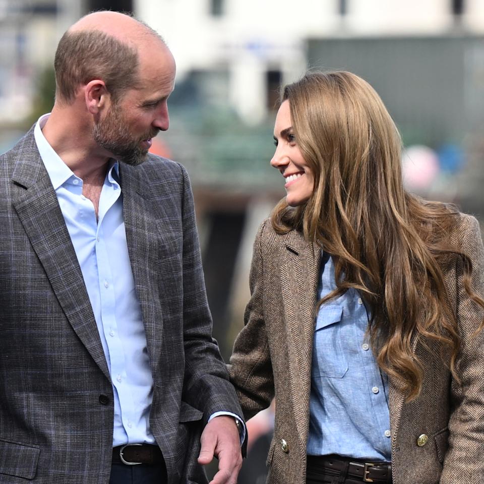 Kate Middleton and Prince William wearing blazers and smiling at each other.