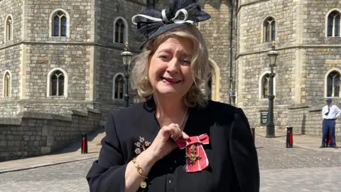 Paul Burrows Wendy Daunt OBE standing outside Windsor Castle with her medal.