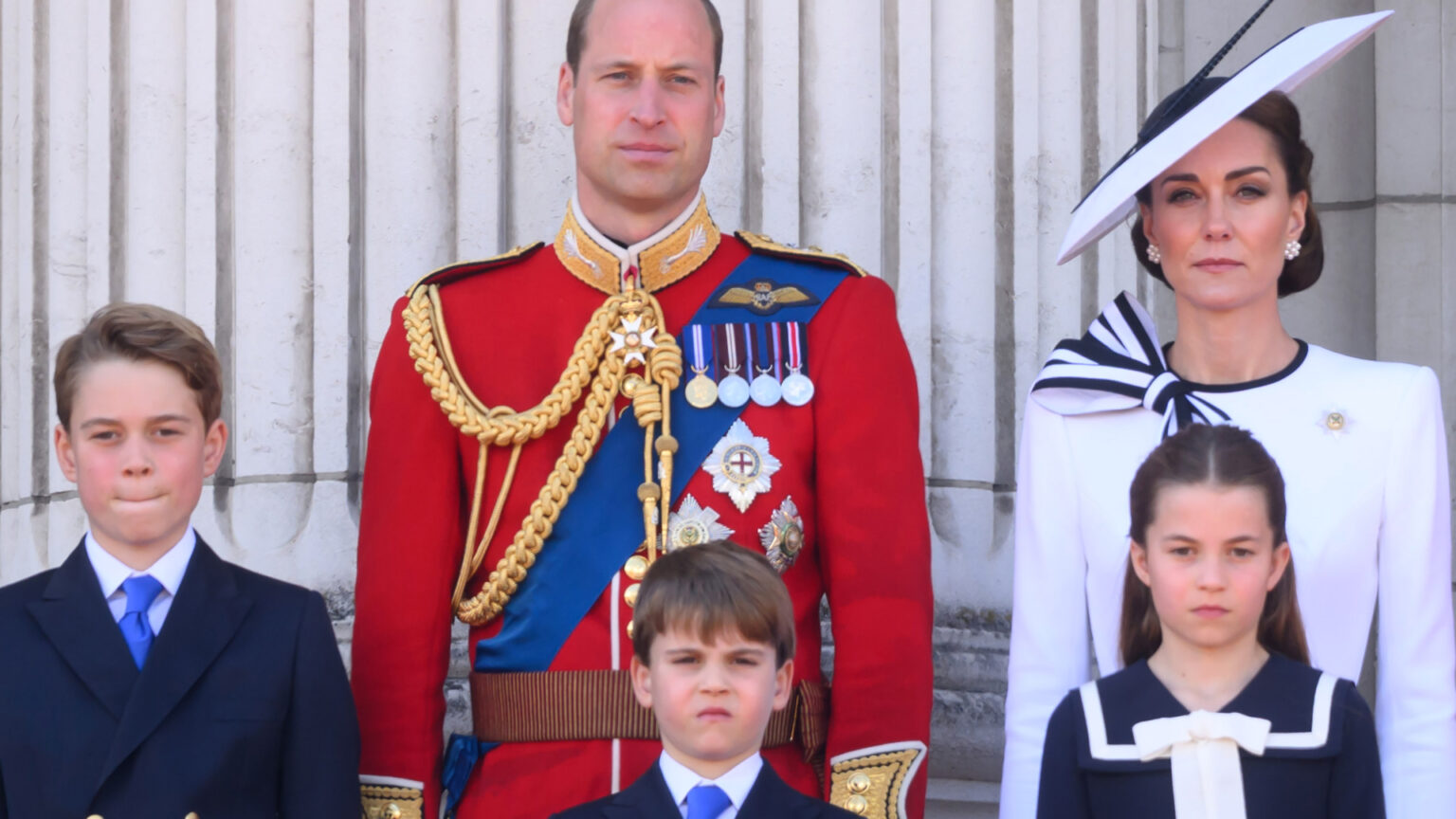How Kate Middleton Is Teaching George, Charlotte, and Louis Prince William wears red military uniform and Kate Middleton wears a white dress with navy detailing, as they stand on the Buckingham Palace with their three kids, Prince George, Prince Louis, and Princess Charlotte