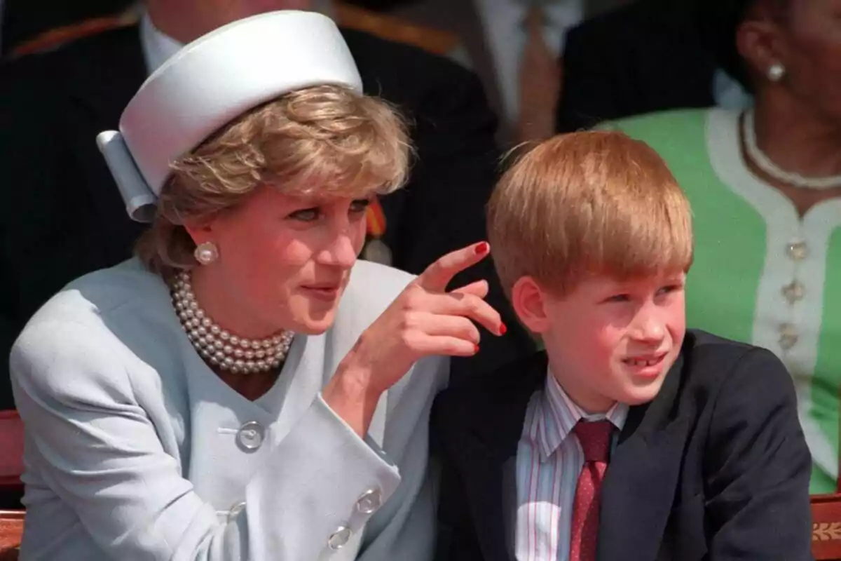 A woman with a hat and pearl necklace is sitting next to a blond-haired child, both looking to the right.