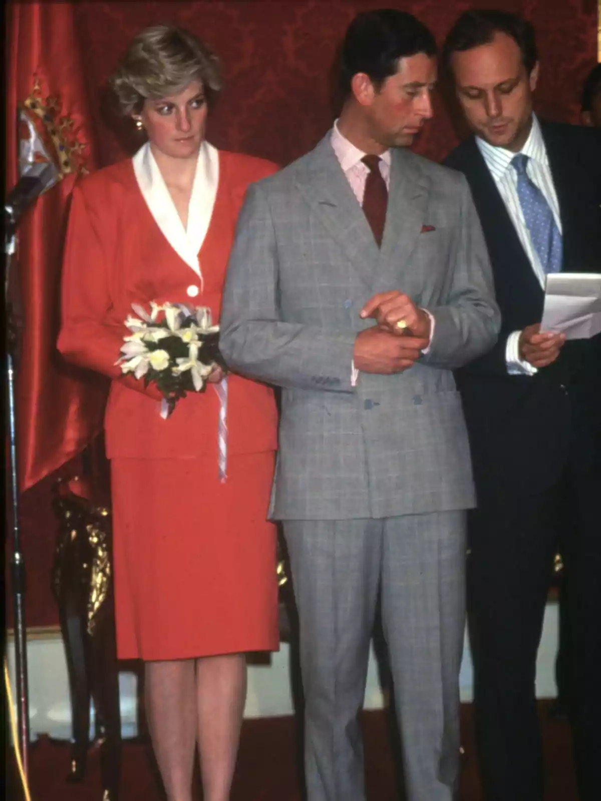 Lady Di with a bouquet of flowers and Charles III in a suit are standing at a formal event. Lady Di with a bouquet of flowers and Charles III in a suit are standing at a formal event.