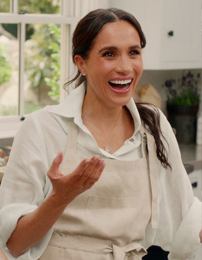 Meghan Markle smiling and wearing an apron in a kitchen setting, related to Vogue cover diva demands. Meghan Markle smiling and wearing an apron in a kitchen setting, related to Vogue cover diva demands.