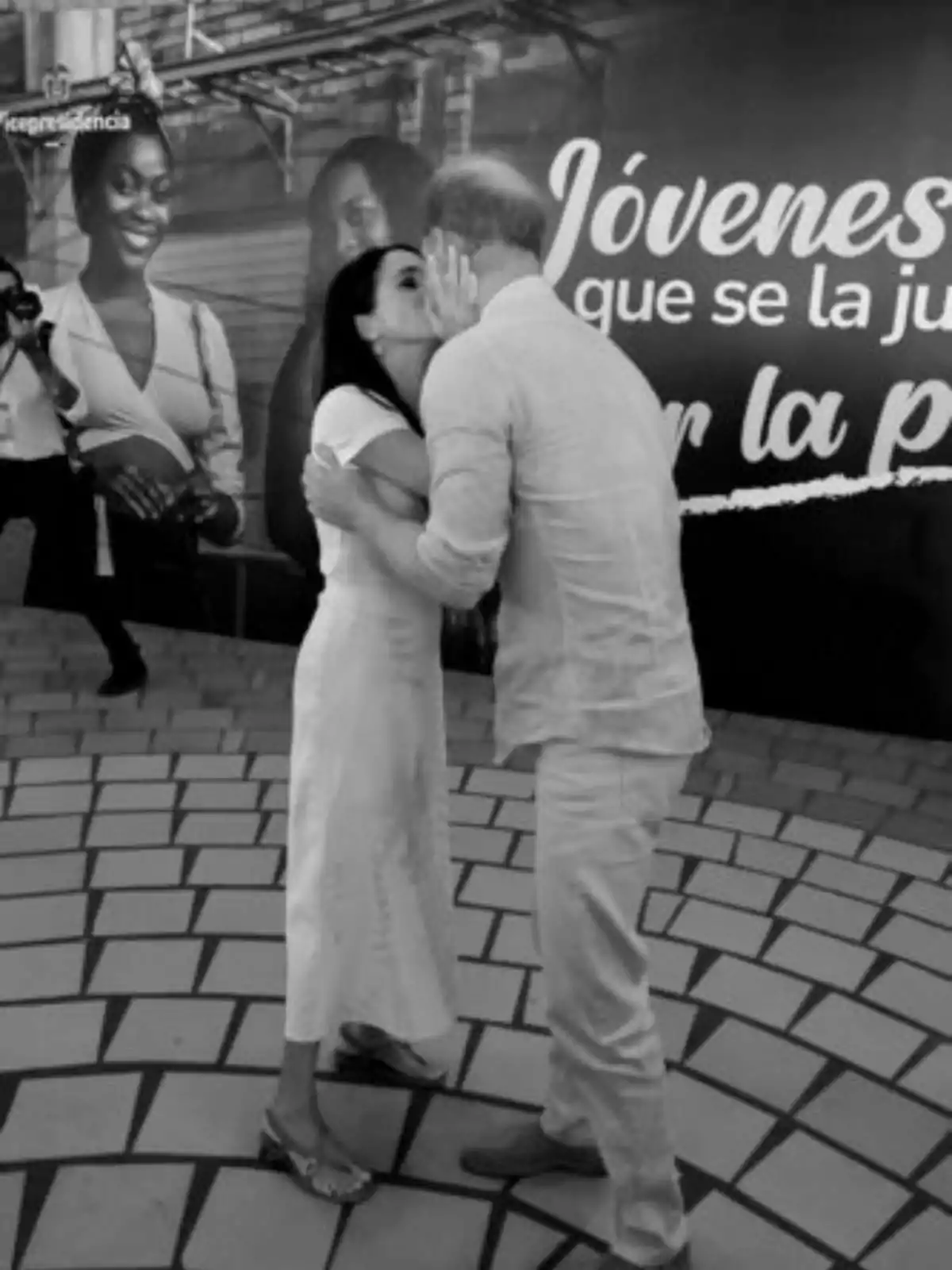 Meghan Markle and Prince Harry hug and kiss on the cheek in front of a sign that reads 