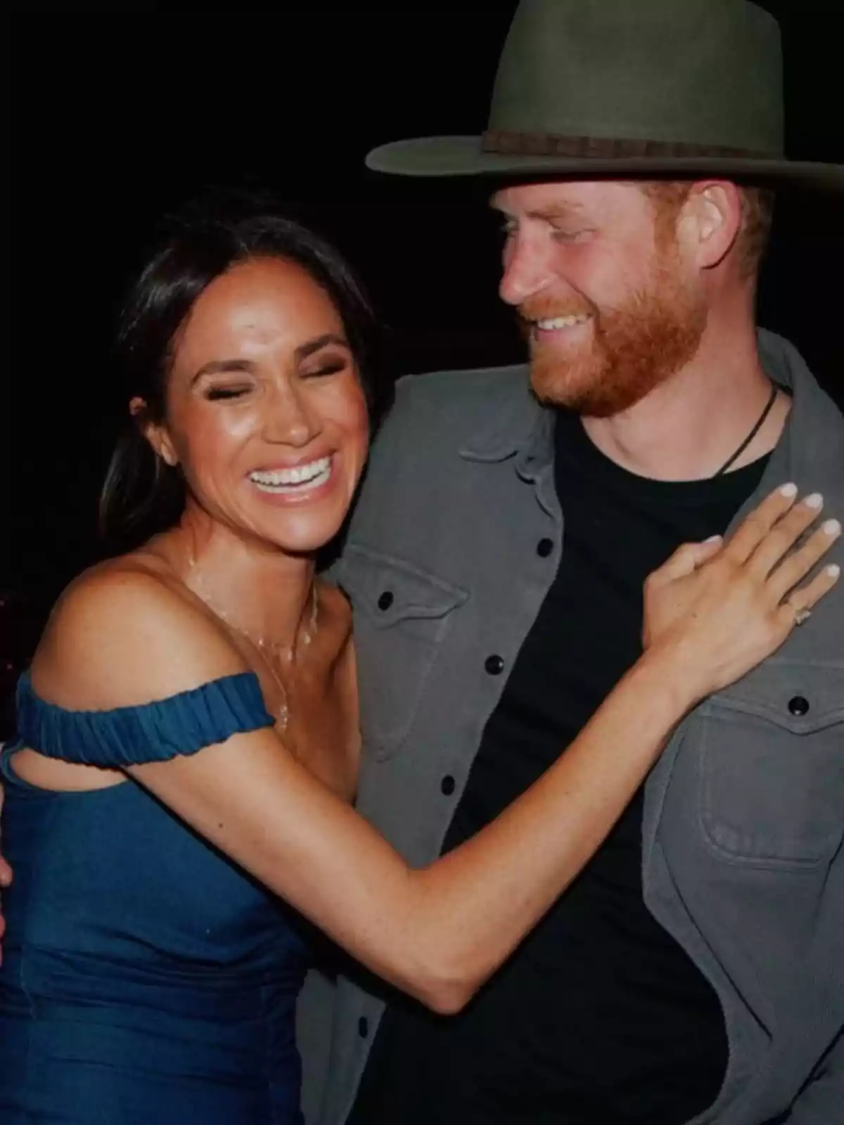 A smiling couple embraces, the woman is wearing a blue dress and the man a green hat.