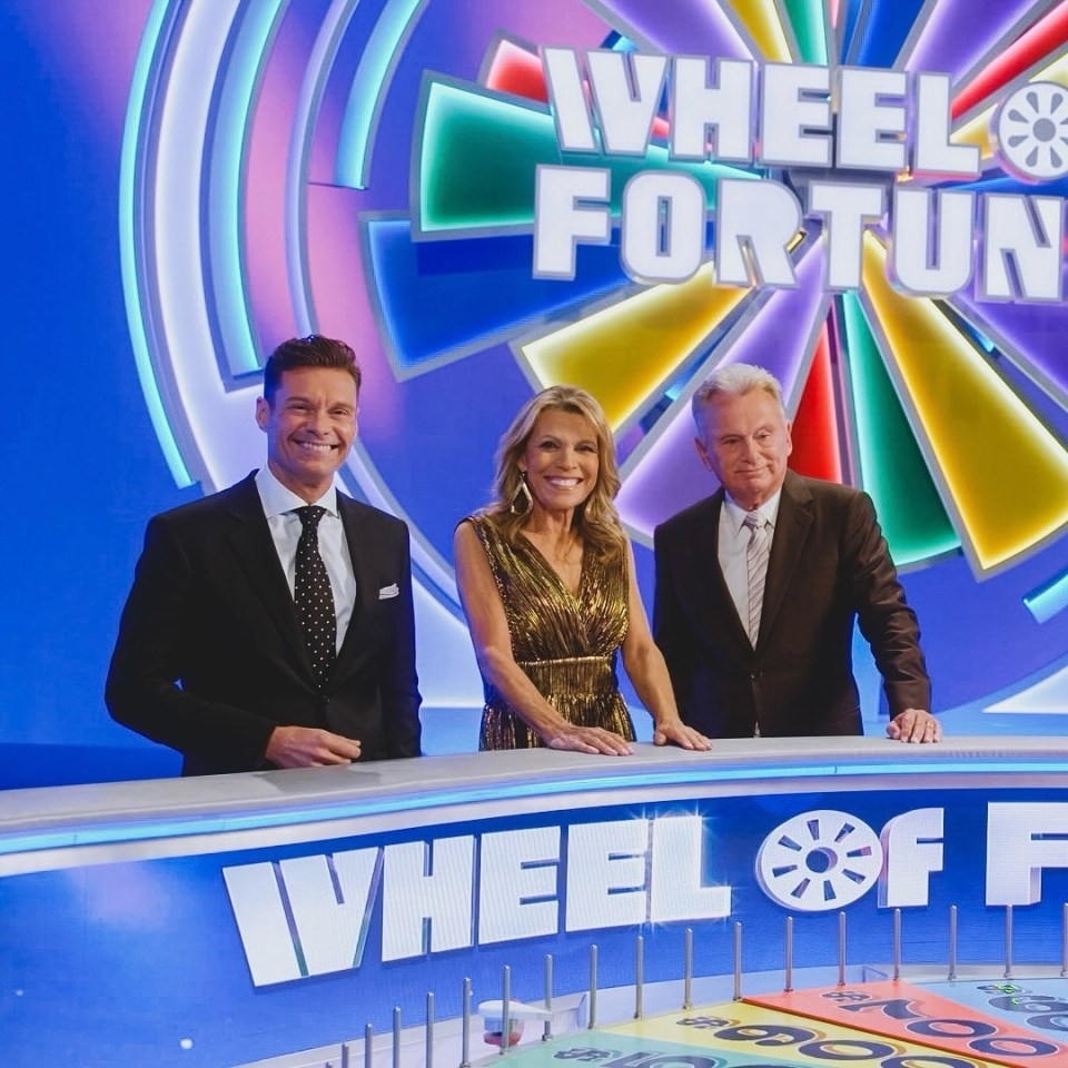Ryan Seacrest, Vanna White, and Pat Sajak on the Wheel of Fortune set.