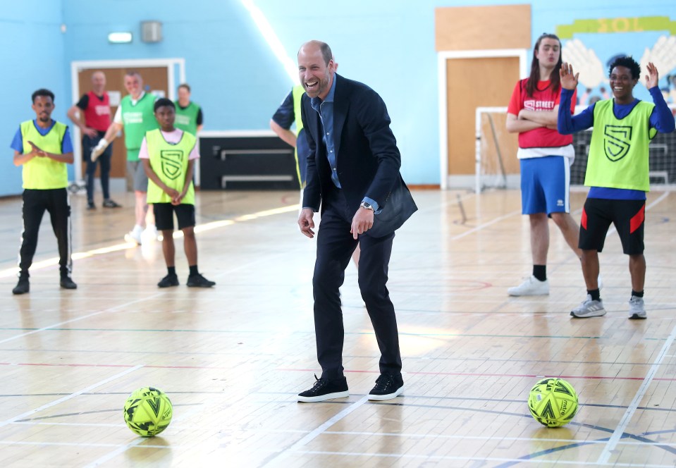 Prince William laughing while playing football with young people.