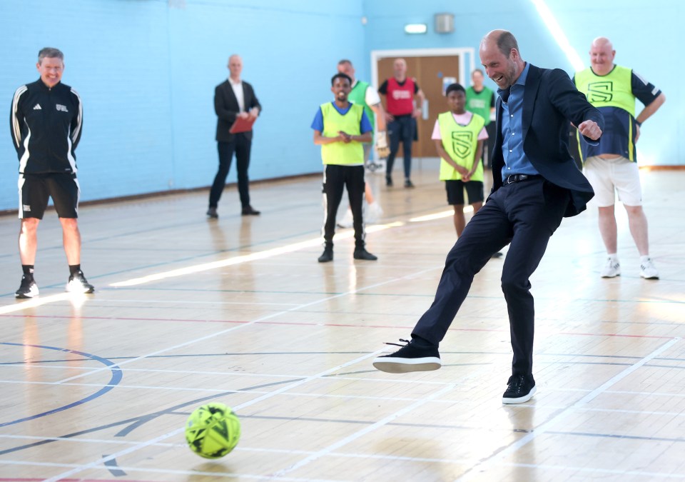 Prince William kicking a soccer ball in a gym.
