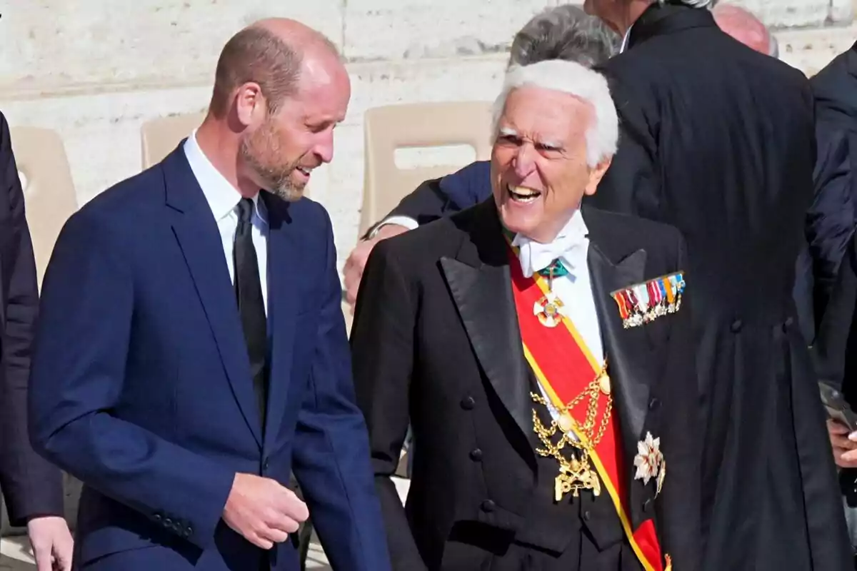 Two men in suits converse and smile - one of them is Prince William - during Pope Francis's funeral.