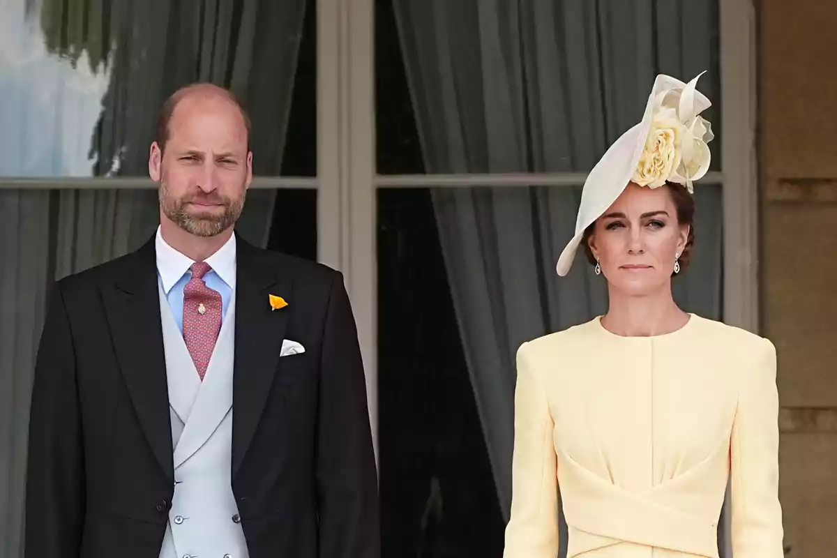 Prince William and Kate Middleton elegantly dressed standing in front of a window with curtains.