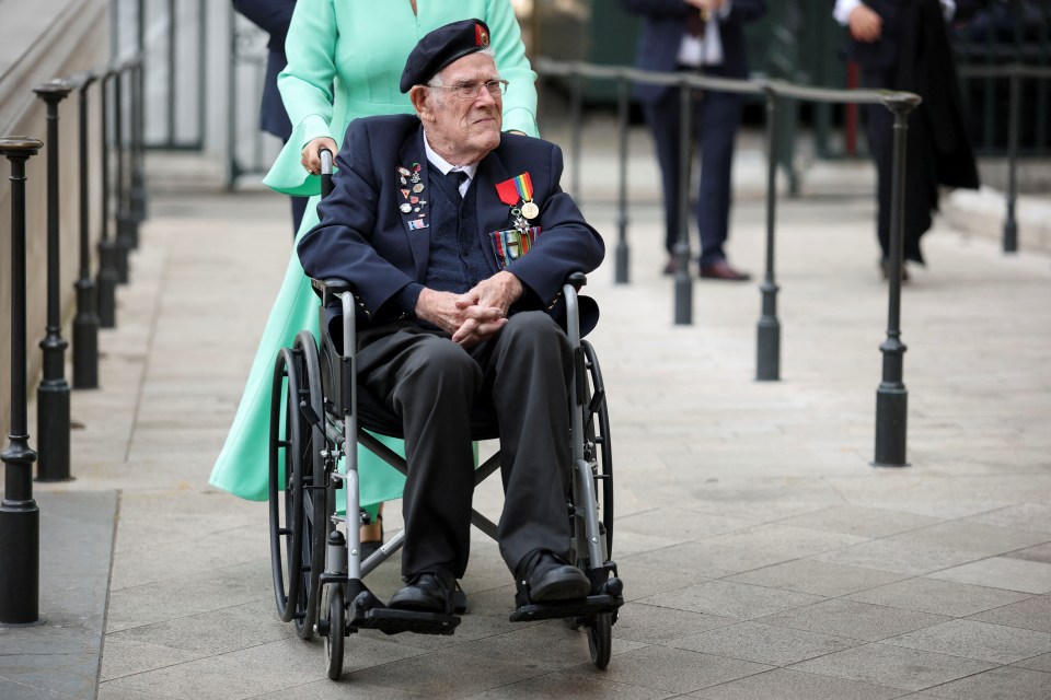 A veteran in a wheelchair, wearing medals, is assisted at Westminster Abbey.
