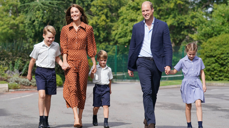 Princess Catherine wearing brown and white polka dot dress with Prince William in blue suit and all three children