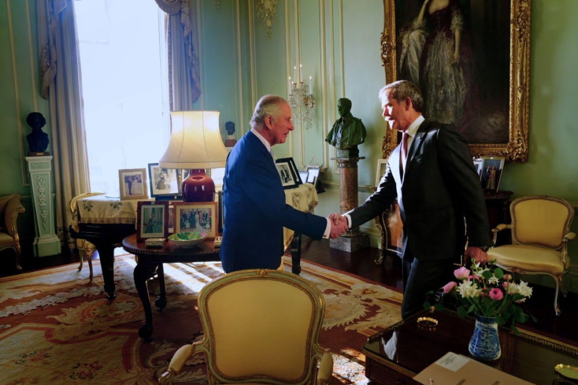 Two people shake hands in a formal room.
