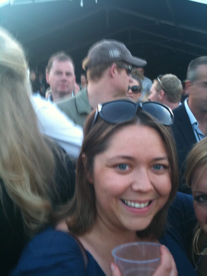 Woman in sunglasses holding a cup, surrounded by people.
