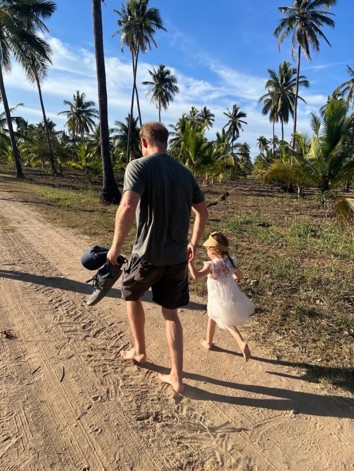 Prince Harry and Lilibet walking barefoot on a dirt road.