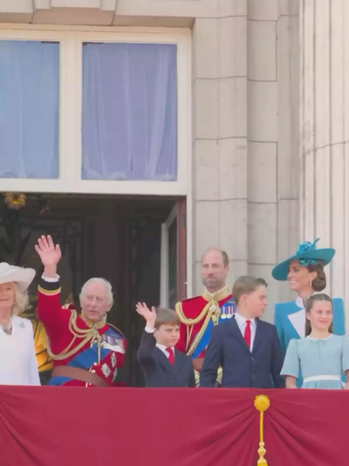 Group of people dressed formally waving from a balcony decorated with red fabric