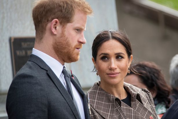 Prince Harry in a grey suit next to Meghan Markle in a checkered jacket.