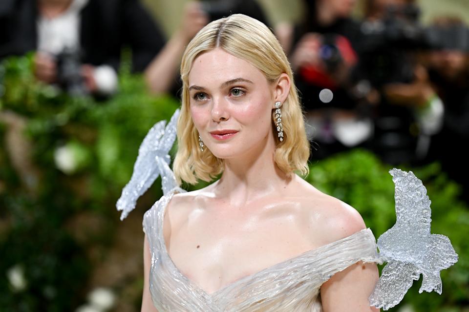 Elle Fanning in elegant gown with butterfly embellishments, posing on event carpet