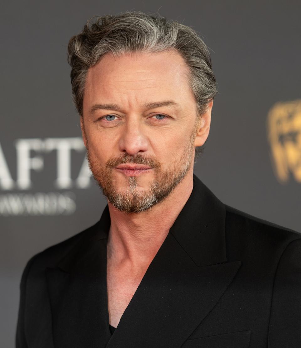 James McAvoy on a red carpet wearing a formal black suit with a subtle beard and styled hair
