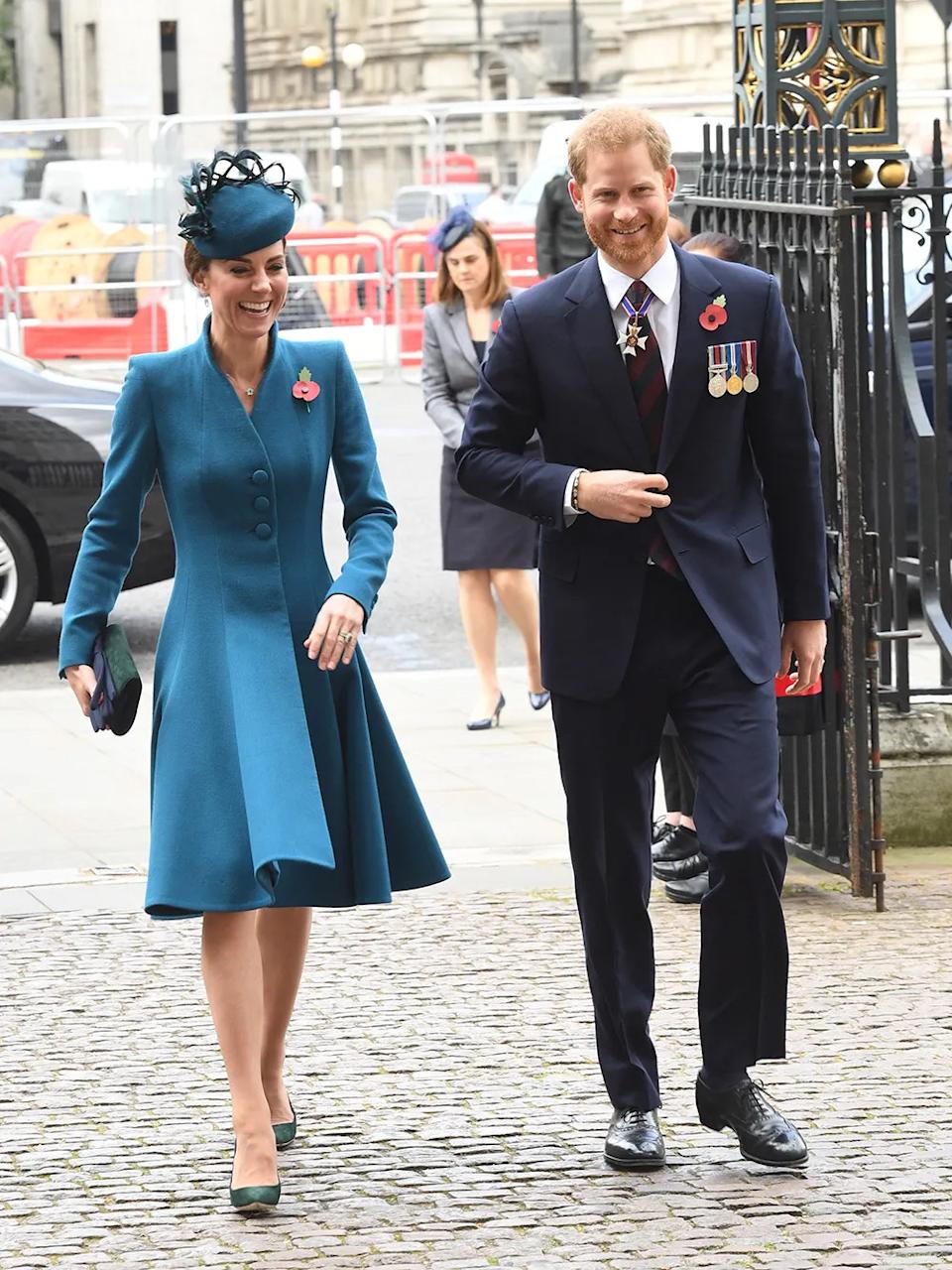 Kate Middleton in a formal blue dress and matching hat walking next to Prince Harry who is wearing a suit with medals.