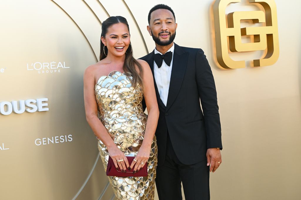 Chrissy Teigen and John Legend in front of a gold background