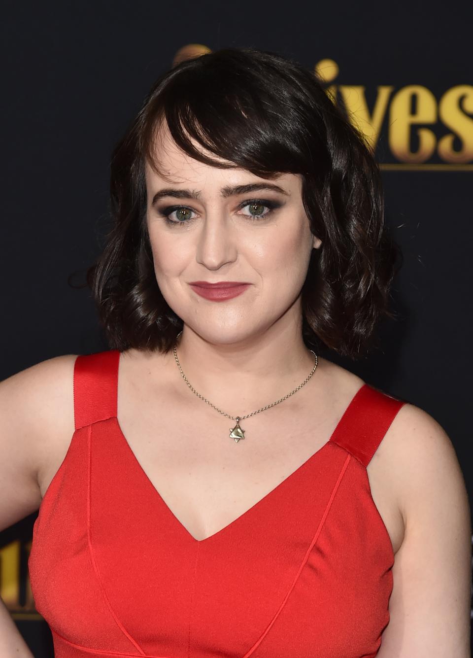 Adult Mara Wilson in a stylish sleeveless red dress poses with a subtle smile at a formal event