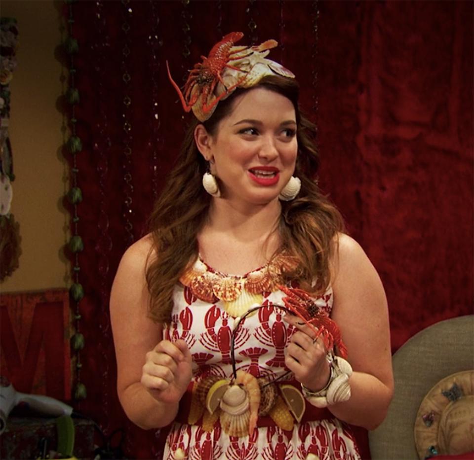 Actress in a lobster-themed dress and matching headpiece, smiling on set with a decorative background