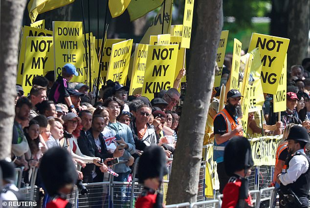 Anti-monarchy protesters stand along the route of the parade holding signs reading 'Not my King'