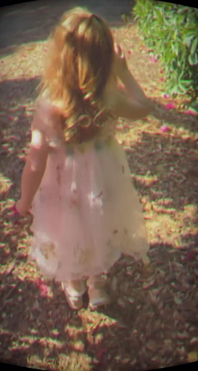 A young Lilibet is seen walking through a wooded area lined with flower petals