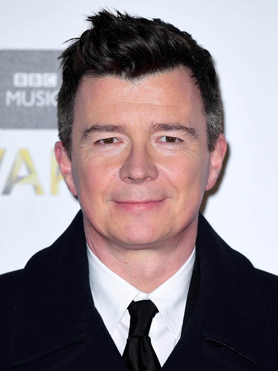 A person in a suit and tie at an event, posing for a photo in front of a backdrop with text