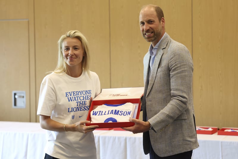 The Prince of Wales hands over a shirt to Leah Williamson during the visit