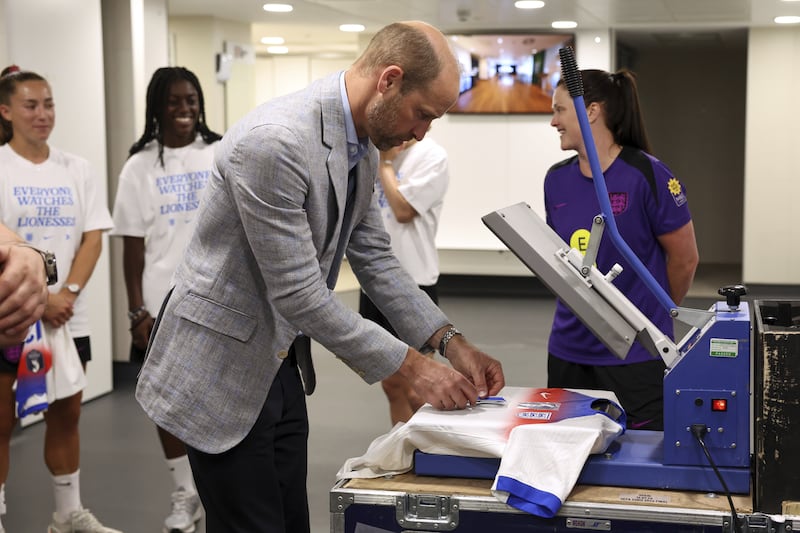 The Prince of Wales prints a number on a shirt as he meets players and coaching staff