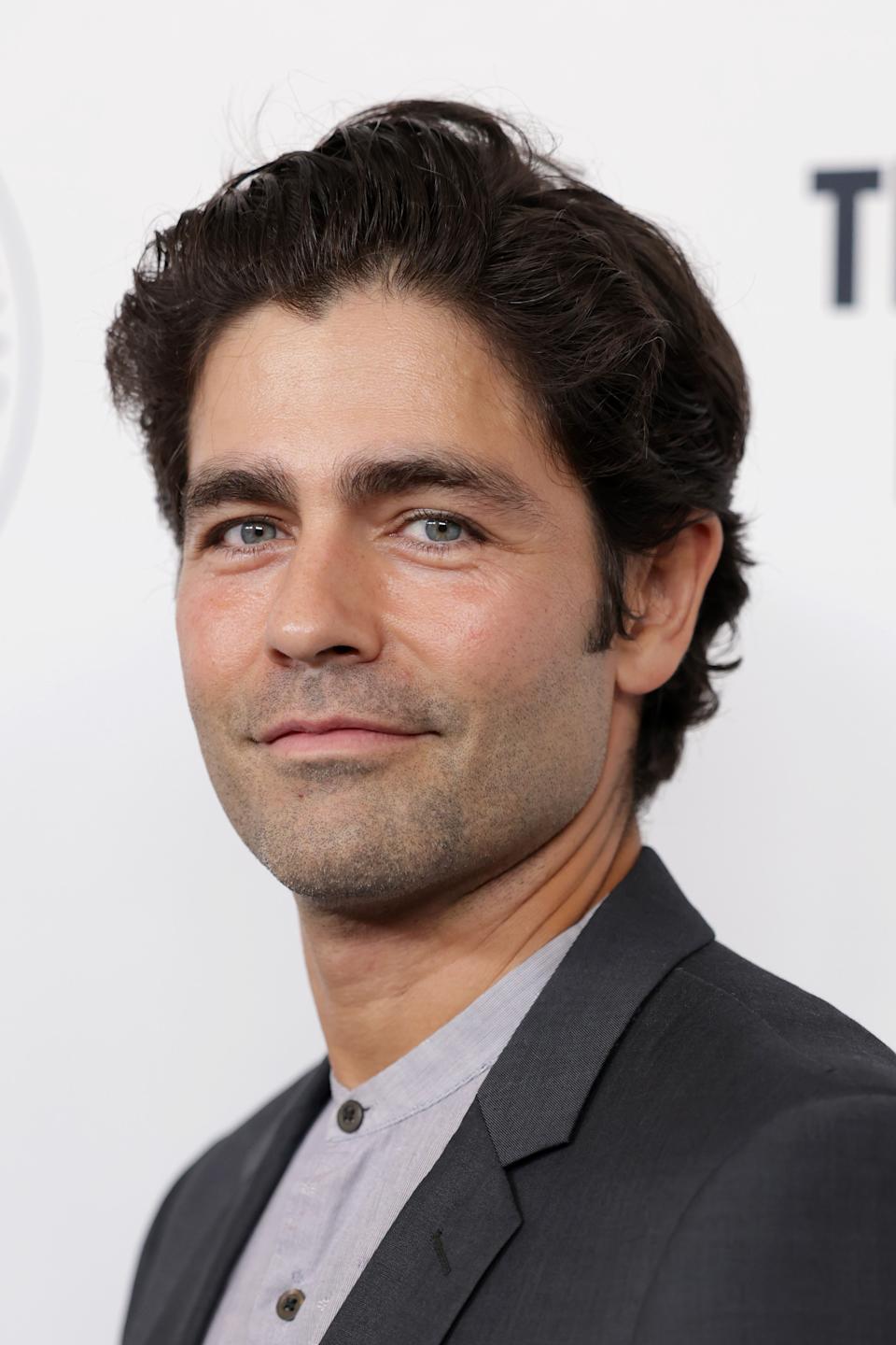 Adrian Grenier a suit and shirt at a formal event, smiling slightly at the camera