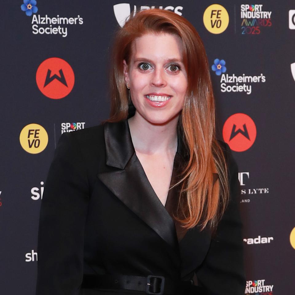 Princess Beatrice smiling wearing a black blazer dress on a red carpet.