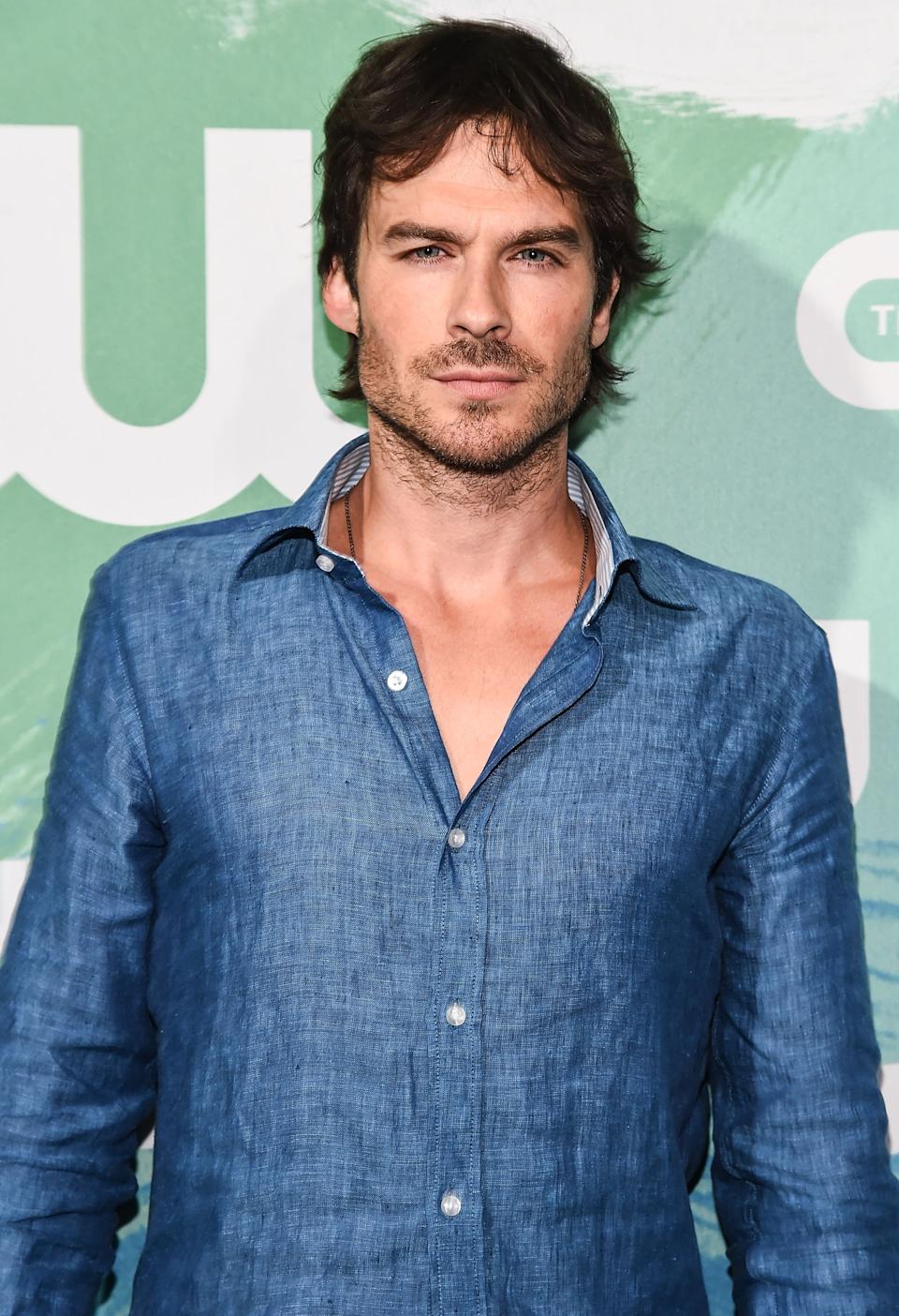 Person in a denim shirt poses at a celebrity event backdrop, exuding a relaxed yet confident style