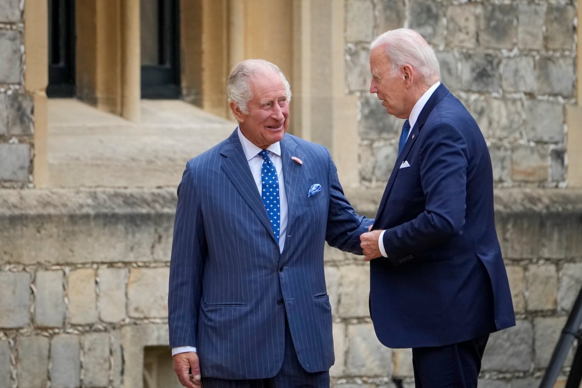 Two people talk with one another in front of a stone building.