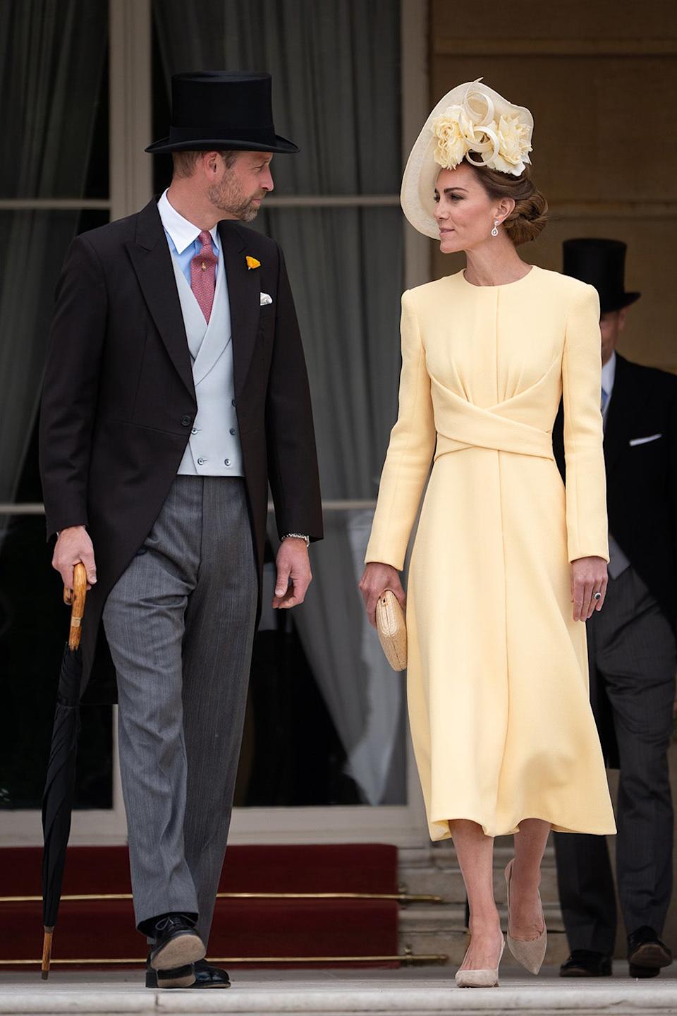 Kate Middleton wearing a butter yellow dress and matching hat walking alongside Prince William in a suit and top hat.
